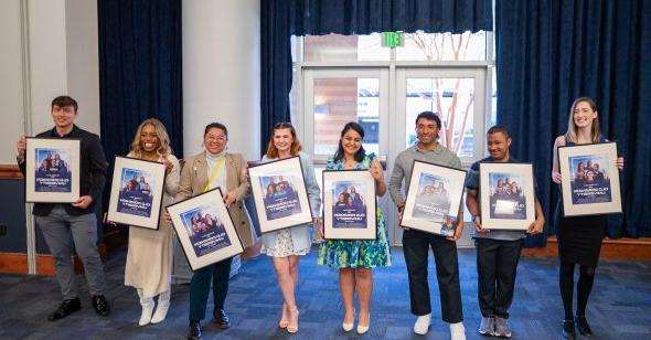 students standing while each holding a framed movie poster 